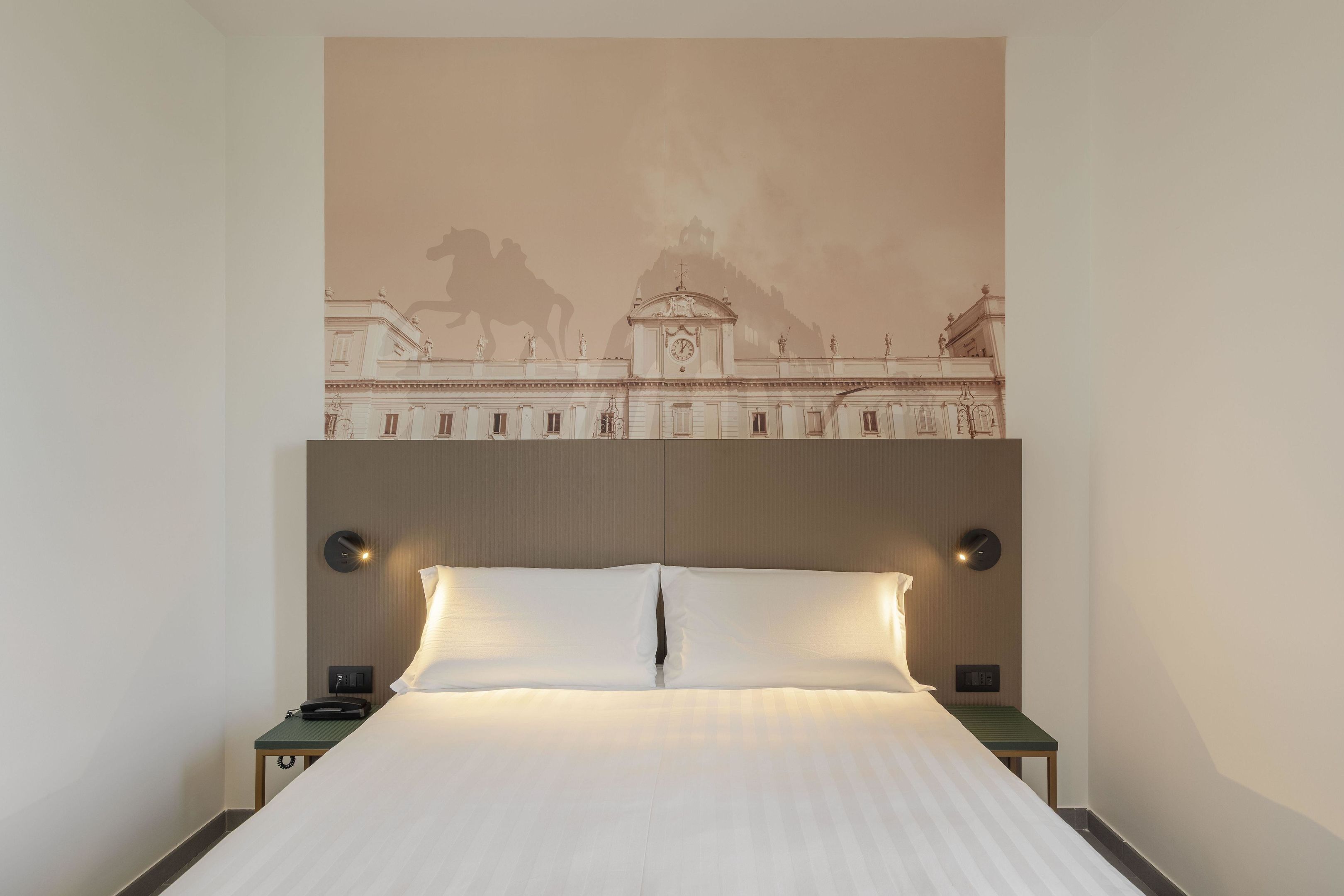 A hotel room with a large bed, two bedside tables, a wall-mounted clock, and a mural of a historical building.