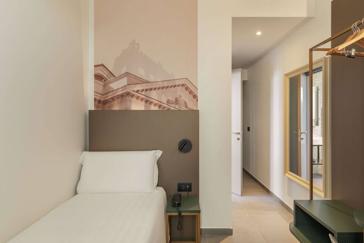 Een hotelkamer met een bed, een nachtkastje met telefoon, een spiegel en een wandklok.