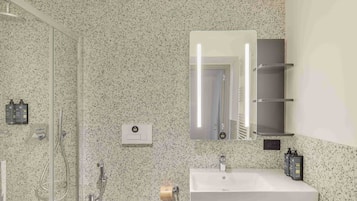 A bathroom with a granite speckled wall, a white sink, a mirror, and a glass shower enclosure.