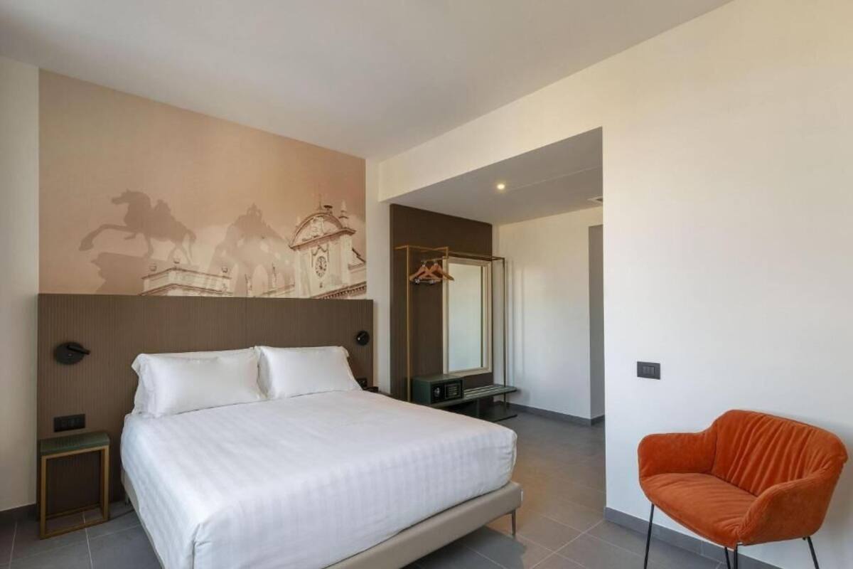 Een moderne hotelkamer met een groot bed, een stoel, een spiegel en een kapstok aan de muur.
