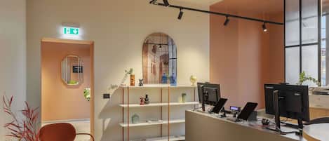 A hotel reception area with a modern design, including a reception desk, computers, and a plant.
