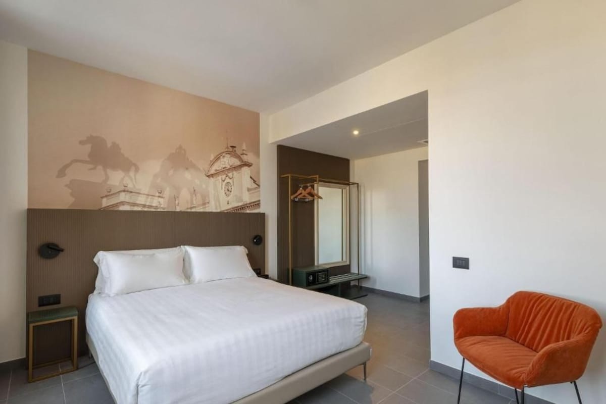 Una habitación de hotel moderna con una cama grande, una silla, un espejo y un perchero de pared.