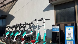 A row of electric scooters parked in front of a building with a signboard.