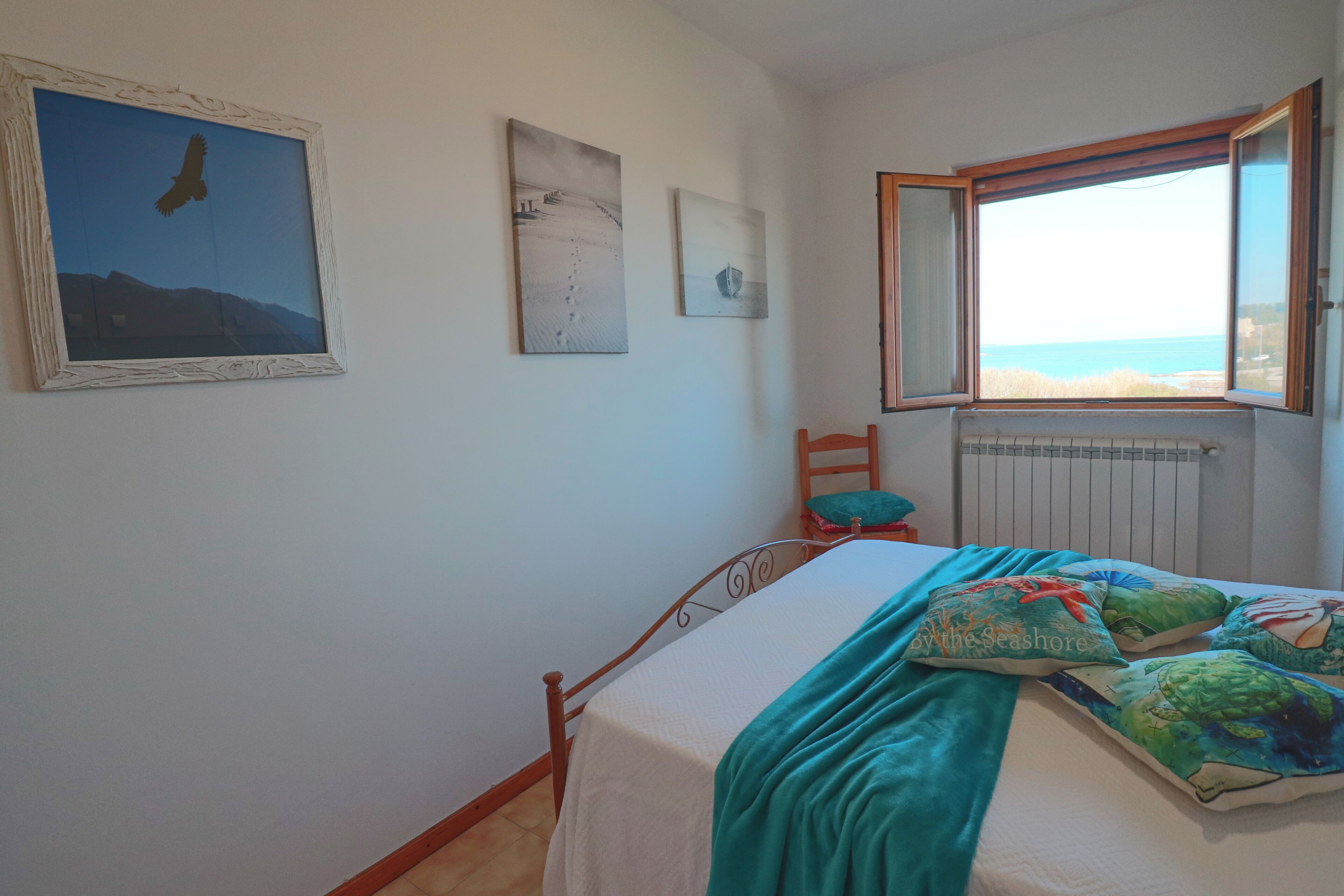 A bedroom with a bed, a window with a view of the sea, and a chair.