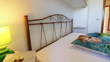 A neatly made bed with a decorative headboard, a bedside lamp, and a pillow with a tropical design.