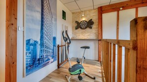 Una habitació amb un ampli quadre de paisatge urbà, un joc de dardo i una bicicleta d'exercici.