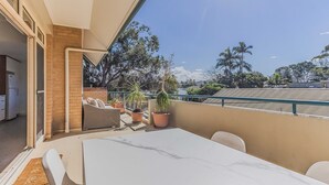Un balcon avec une table et des chaises, des plantes en pot et une vue sur les arbres et les bâtiments.