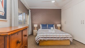 A bedroom with a bed, a wooden dresser, a brick wall, and a ceiling fan.