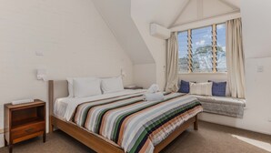 Une chambre à coucher avec un lit, une table de chevet, une fenêtre avec des rideaux et un radiateur.