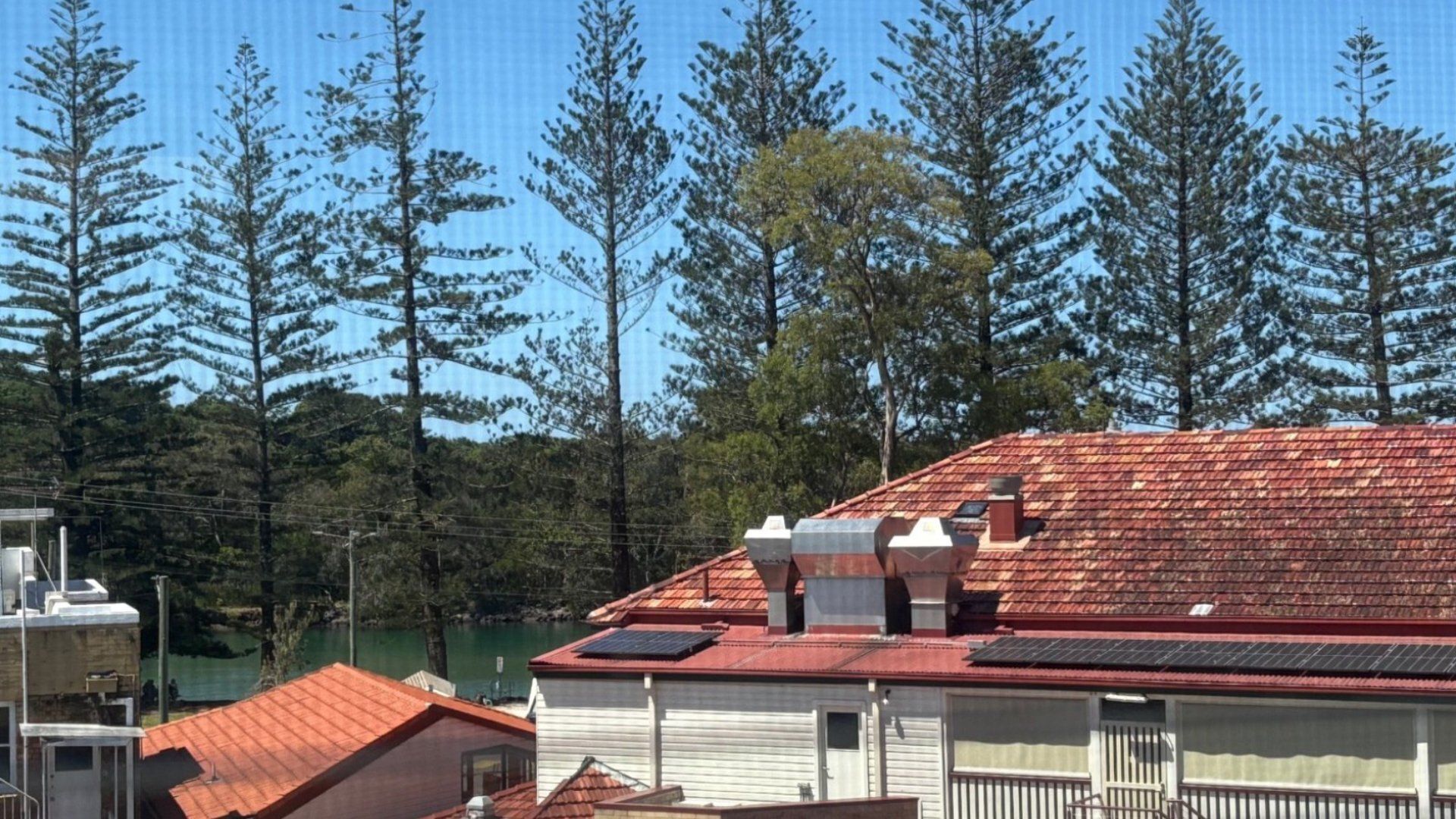 Ein Wohngebäude mit rotem Ziegeldach, Solaranlagen und Blick auf hohe Bäume.