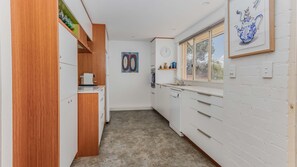 Une cuisine étroite avec des meubles blancs, un meuble en bois, une machine à café et une fenêtre donnant sur un beau paysage.