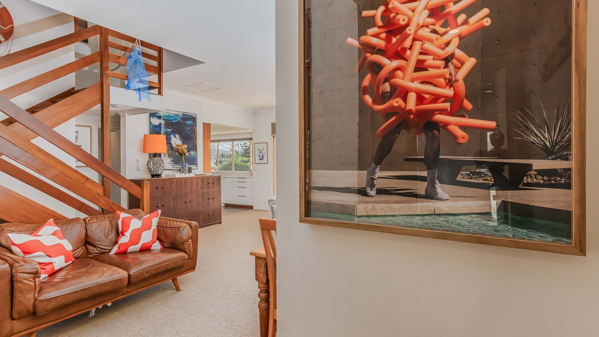 A modern living room with a brown leather sofa, a wooden staircase, and a large abstract painting.