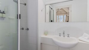 Une salle de bain avec une porte de douche en verre, un lavabo blanc avec un miroir au-dessus, et une bouteille de shampoing posée sur le lavabo.