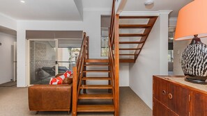 A staircase with a wooden finish, a leather sofa with a red and white cushion, and a wooden cabinet with a decorative vase.