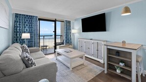 Un salon comprenant un canapé, une table basse, un téléviseur et donnant sur l’extérieur.