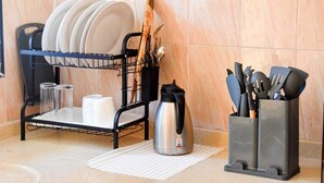 Un espacio de cocina con un escurreplatos que contiene platos y tazas, una tetera y un recipiente para utensilios.