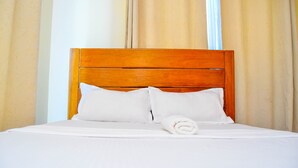 Una cama bien hecha con sábanas y almohadas blancas, un cabecero de madera y una toalla enrollada sobre la cama.