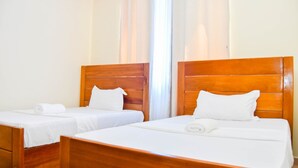 Dos camas de madera con sábanas y almohadas blancas, un cabecero de madera y una ventana con cortinas.