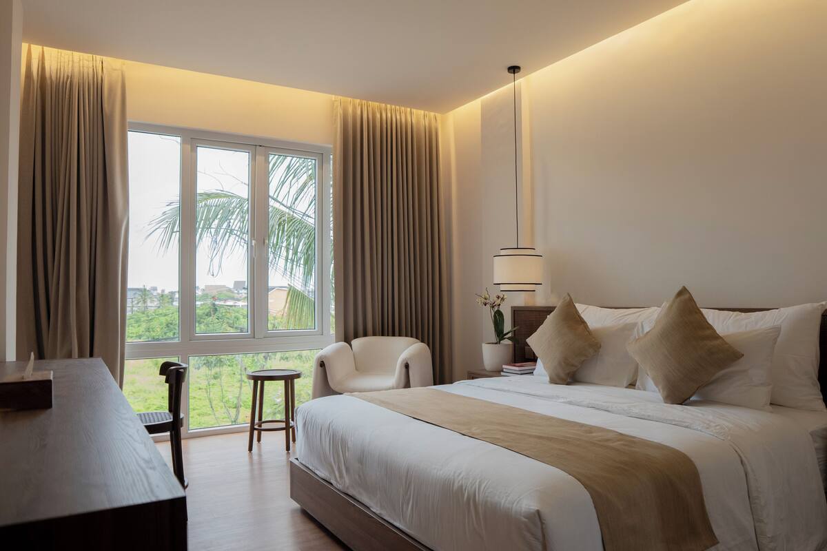 Habitación de hotel con una cama grande, un escritorio, una silla y vistas al exterior.