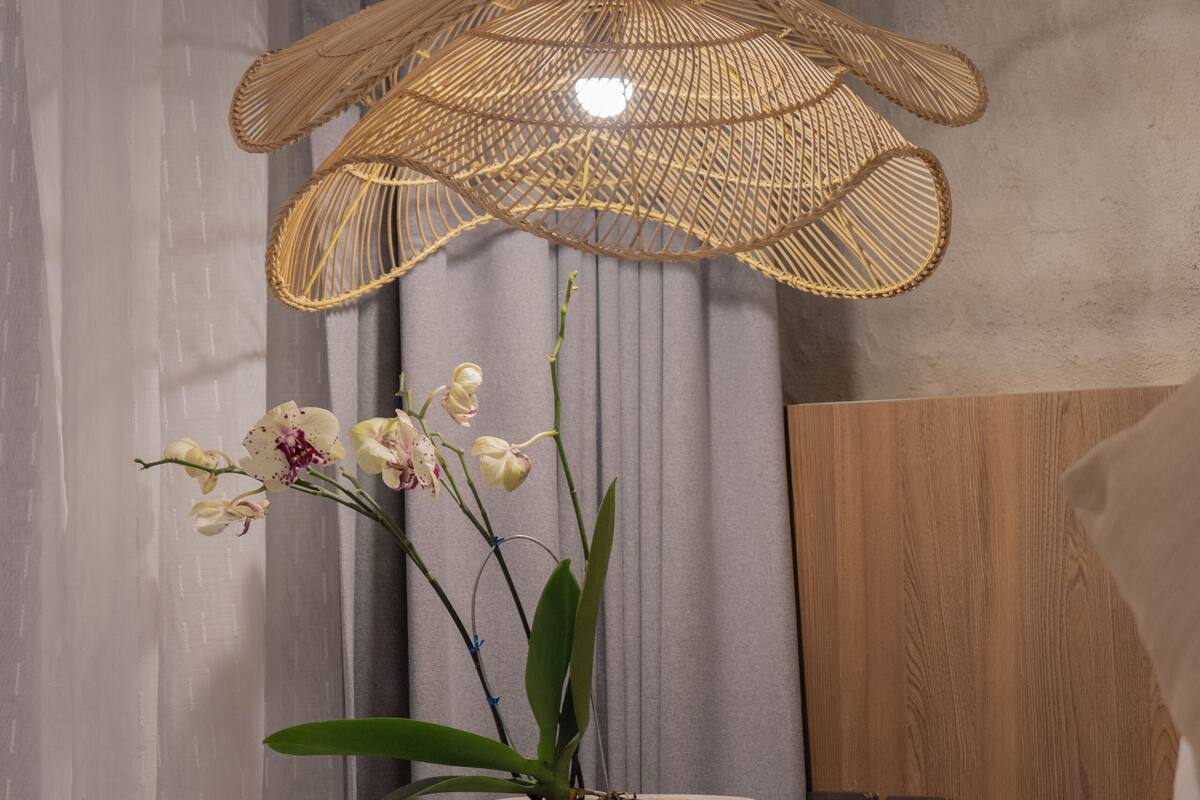 Una cama con una colcha blanca, una lámpara de mimbre y una orquídea en maceta.
