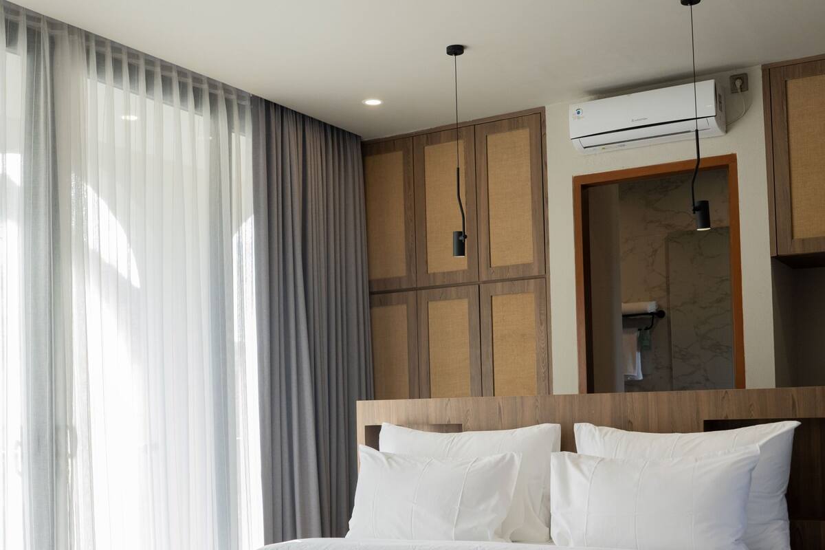 Una habitación de hotel moderna con una cama grande, cabecera de madera y aire acondicionado instalado.