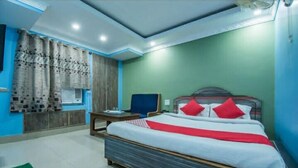 A hotel room with a bed, a desk, a chair, and a window with curtains. - HOTEL MUNDRIKA DELUXE (Patna)