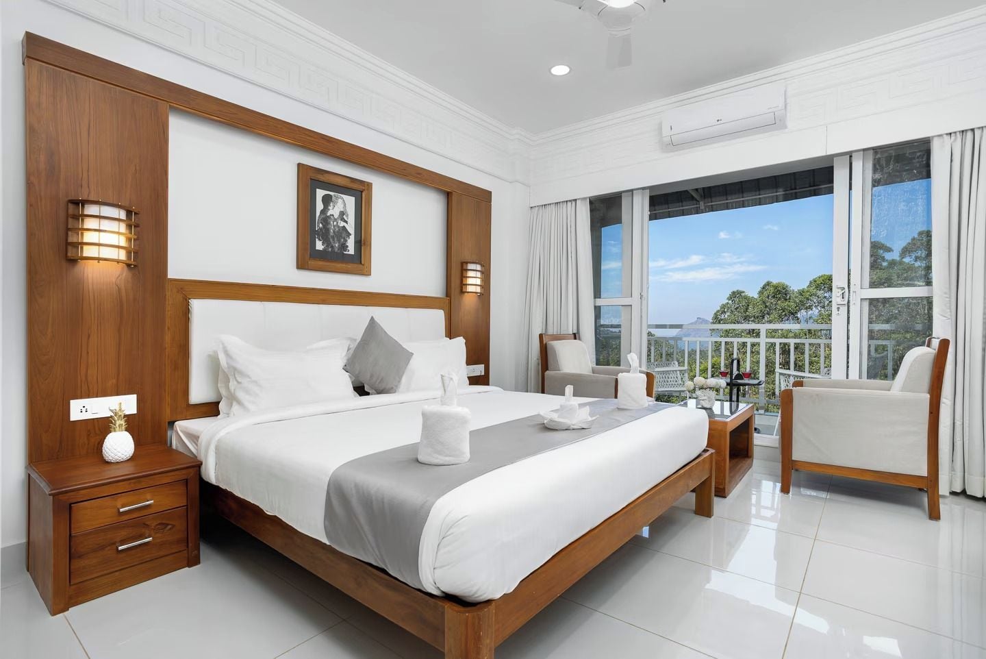 Habitación de hotel con una cama grande, un espacio para sentarse con una silla, un balcón con vistas y un cabecero de madera.