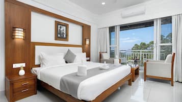 Habitación de hotel con una cama grande, un espacio para sentarse con una silla, un balcón con vistas y un cabecero de madera.