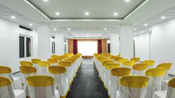 Un salón de conferencias con filas de sillas, lazos blancos y amarillos, y un suelo oscuro.