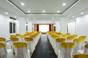Un salón de conferencias con filas de sillas, lazos blancos y amarillos, y un suelo oscuro.