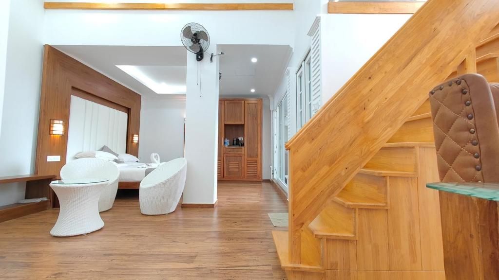 A hotel room with a wooden staircase, a bed with white bedding, a small table, and a fan.