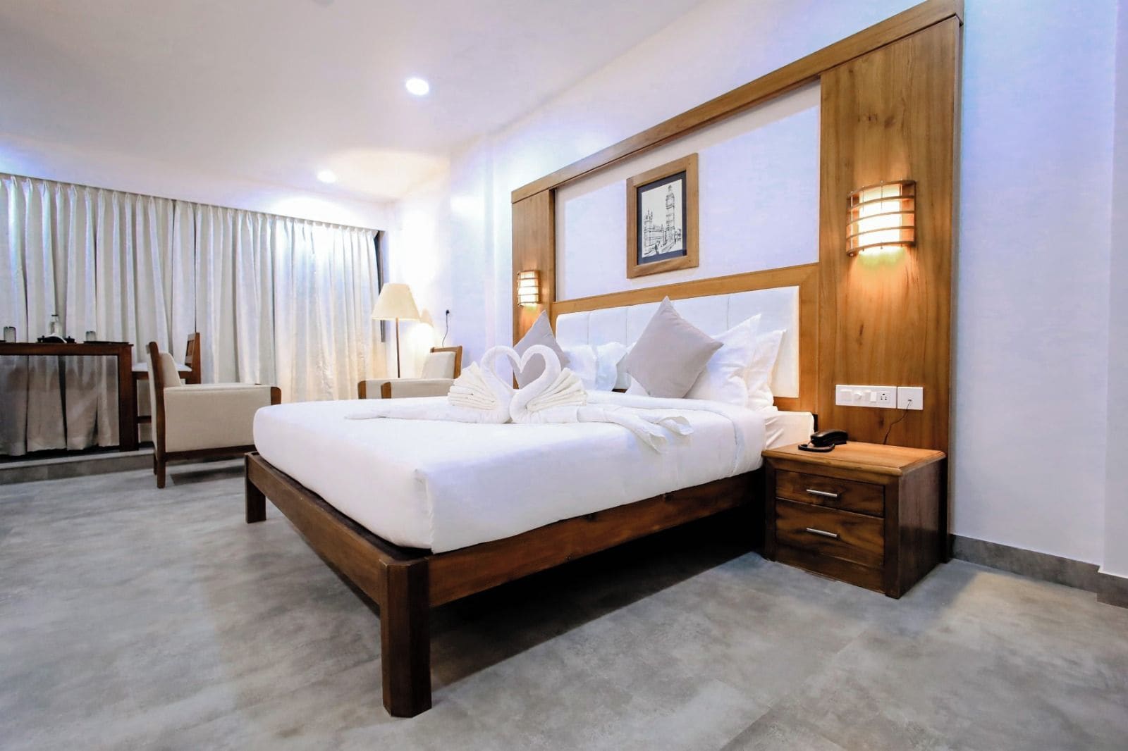 A hotel room with a large bed, wooden headboard, bedside lamps, a desk, and a chair.