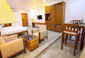Habitación de hotel con cama, dos sillones, una mesita de centro, un escritorio, un televisor y un armario.