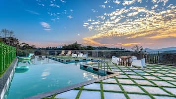 Una piscina en la azotea con vistas a la puesta de sol y montañas distantes.