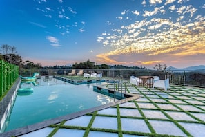 Una piscina en la azotea con vistas a la puesta de sol y montañas distantes.