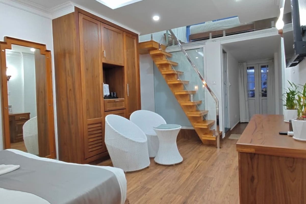 Habitación de hotel con cama, armario de madera, un pequeño espacio para sentarse, una escalera y una planta en maceta.