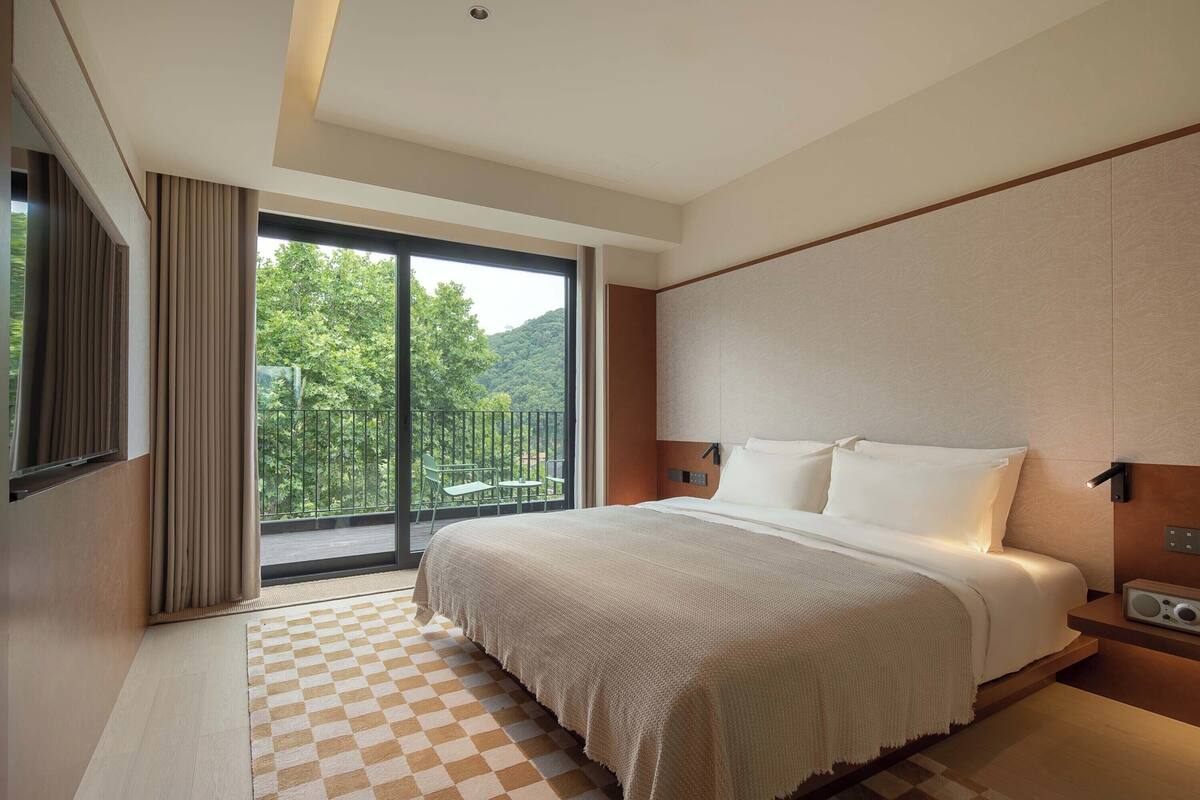 Habitación de hotel moderna con una cama grande, televisión y balcón con vistas a zonas verdes.