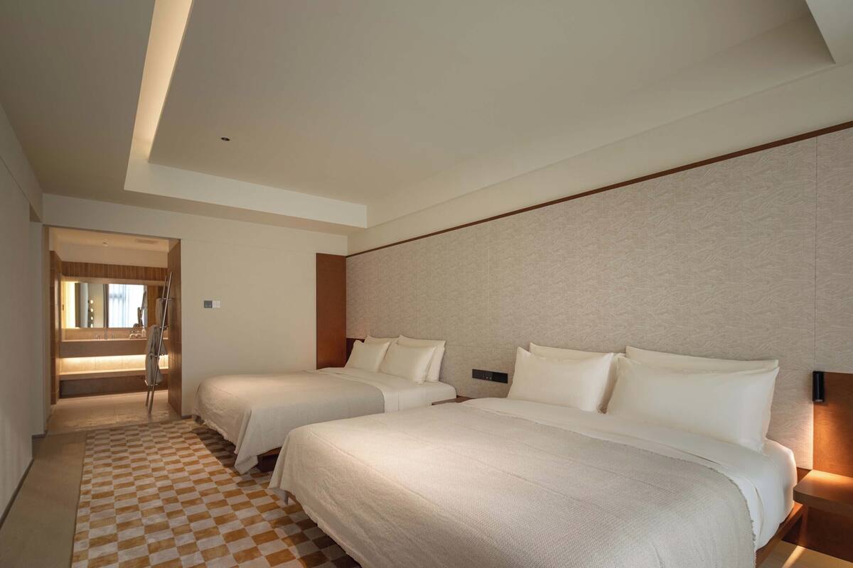 Habitación de hotel con dos camas, piso a cuadros, baño con espejo y cabecera de madera.