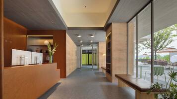 A modern reception area with a wooden reception desk, a bench, and a view of the outdoor seating area.