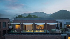 A modern building with a rooftop pool area, large windows, and a view of surrounding hills. - Árbol Moganshan Yucun (Huzhou)