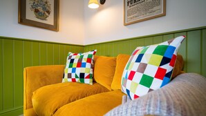 Un sofá amarillo con almohadas de cuadros coloridos, una obra de arte floral enmarco y un panel de pared verde.