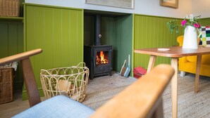Una habitación acogedora con una pared verde, una mesa de madera, una silla de mimbre y una pequeña chimenea.