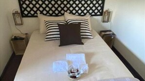 Una cama bien hecha con almohadones a rayas, un cojín decorativo oscuro y una pequeña cesta con artículos de aseo sobre la cama.