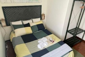 Ein Bett mit kariertem Überwurf, ein Kopfteil mit gepunktetem Muster und ein Nachttisch mit Lampe.