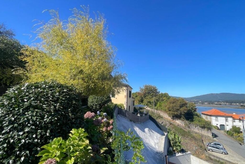 A hillside property with a view of the sea, a paved path, and a building with a red roof.