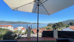 Una terraza con vista a un lago y colinas distantes, un paraguas grande y suelo de baldosas.
