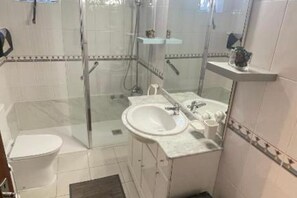 Ein Badezimmer mit Duschkabine aus Glas, Toilette, Waschbecken mit Spiegel und Ablagefläche für Toilettenartikel.