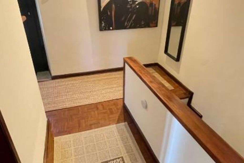 A hallway with wooden flooring, a carpeted area, and a wooden handrail.