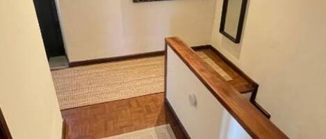 A hallway with wooden flooring, a carpeted area, and a wooden handrail.