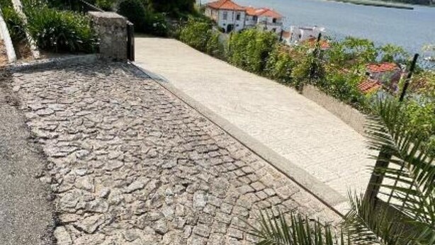 Un camino empedrado que lleva a un edificio con vista a un río y casas al fondo.